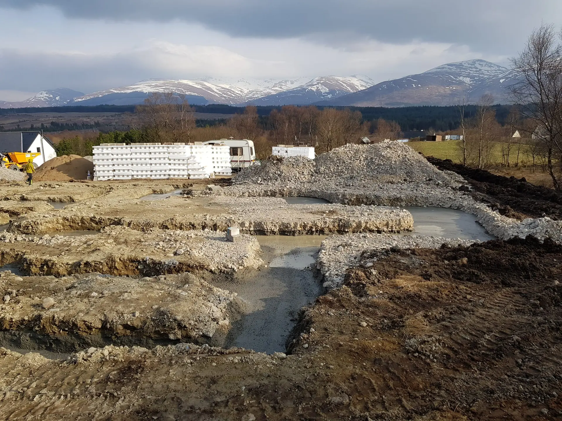 Foundation trenches poured, with snow-capped mountains beyond