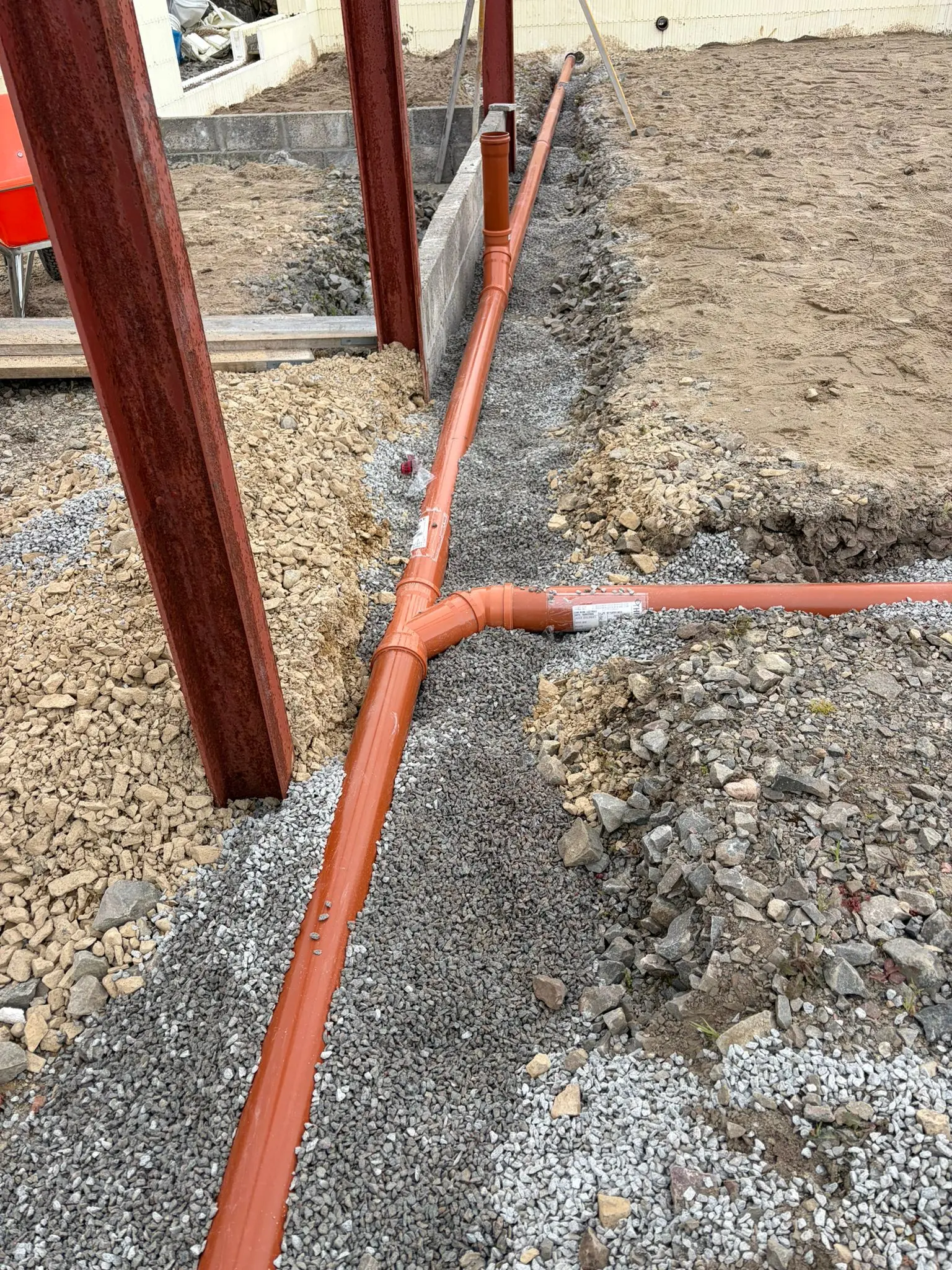 Drainage pipe junction bedded in gravel beside the steel columns